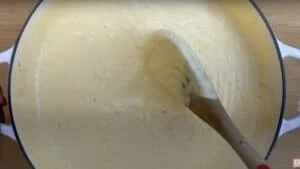 Creamy cheese sauce being stirred in a pot with a wooden spoon, perfect for pasta or dipping.